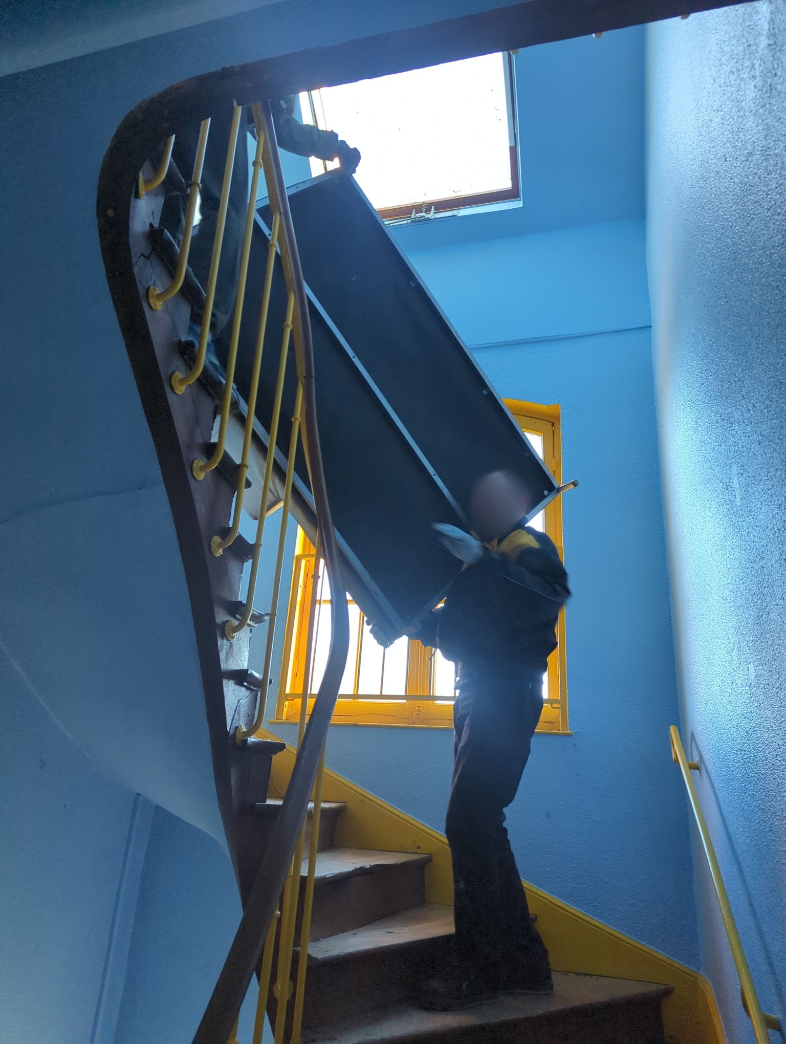 View from below of two people moving a sofa during a move in a narrow staircase.